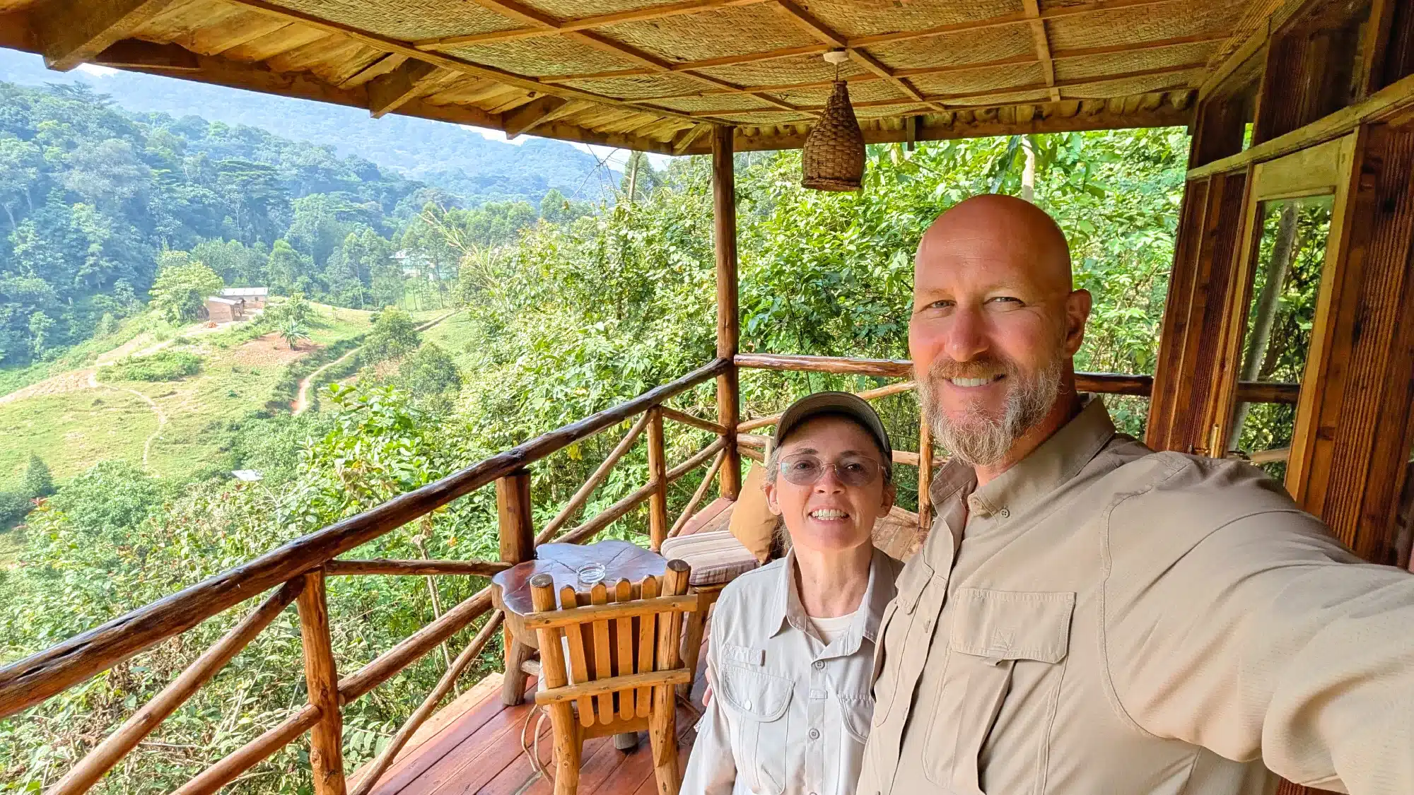 Barton Jeffs and his wife Tracy Jeffs, founders of All in Africa Safaris USA, smiling on a wooden lodge balcony overlooking a lush green African forest
